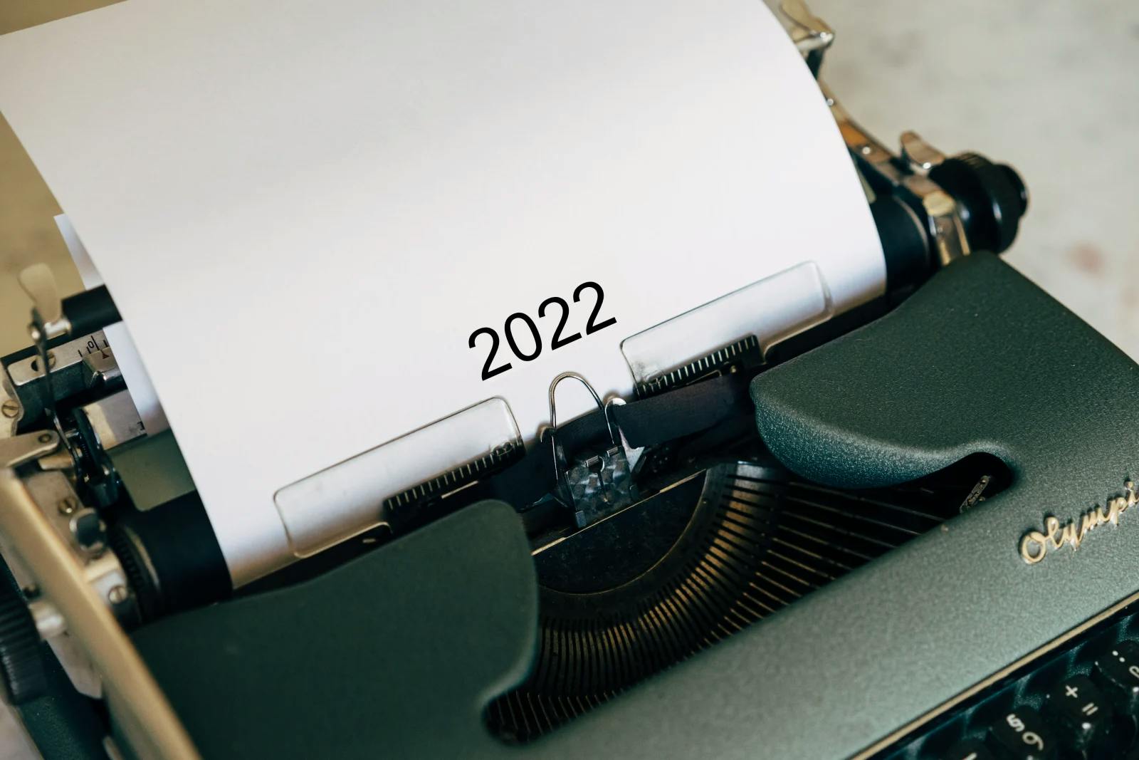 A classic brown, grey, black, and green typewriter with a single sheet of paper in it that says boldly, 2022